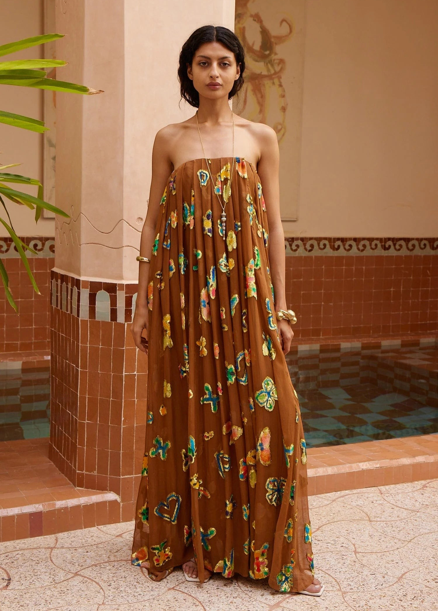 KABE SHOP INC strapless midi gown in brown with vibrant butterfly patterns, worn by a model in a tiled courtyard.