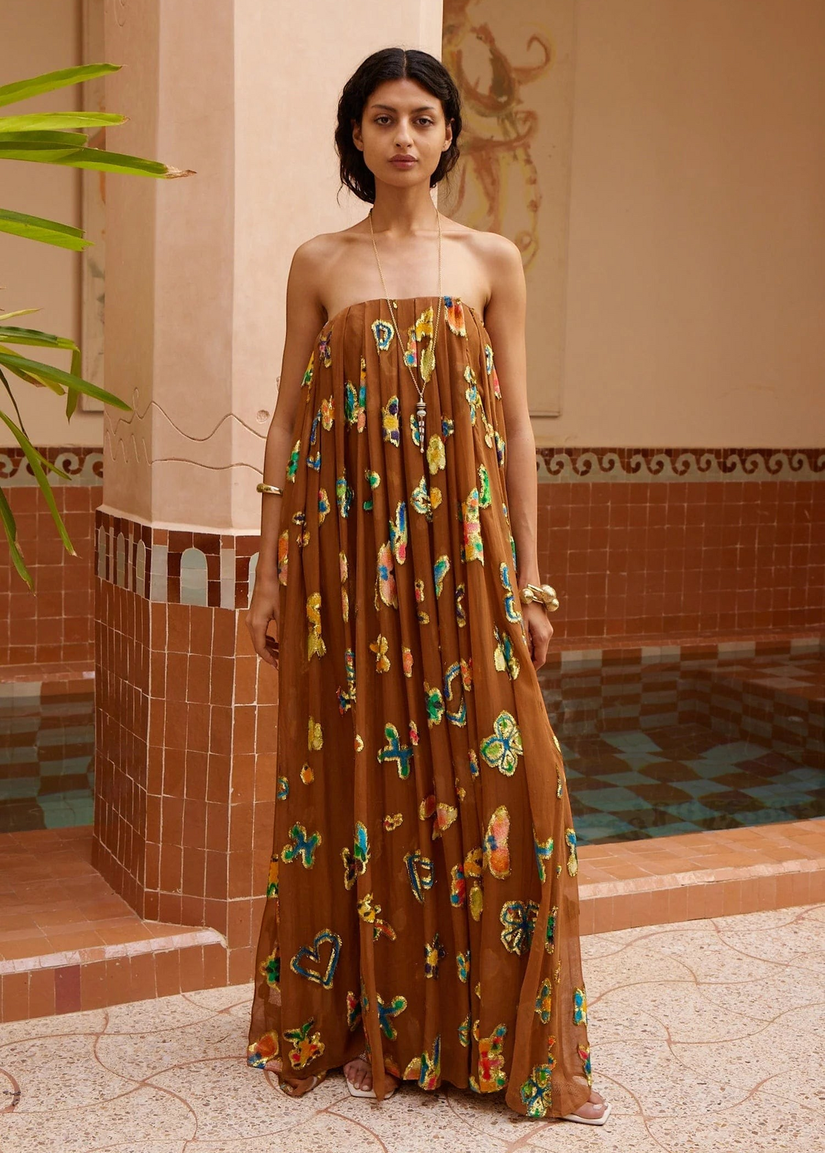 KABE SHOP INC strapless midi gown in brown with vibrant butterfly patterns, worn by a model in a tiled courtyard.