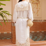 KABE SHOP INC Rosemary midi dress in white linen with intricate lace trim, worn with a straw hat and woven bag.