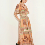 Model wearing KABE SHOP INC Alberta midi shirtdress in orange with tropical print, cinched waist, and collar detail.