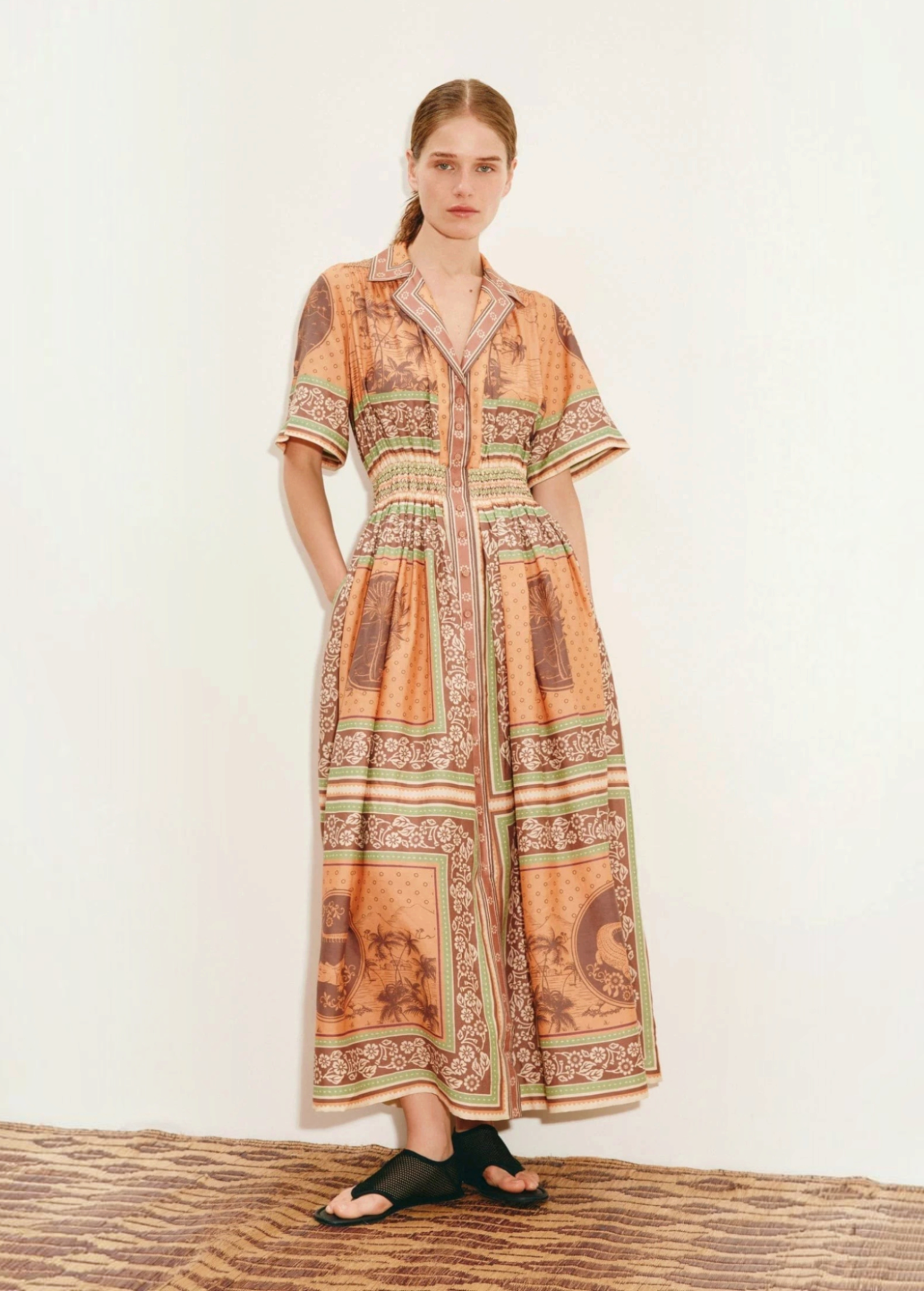 Model wearing KABE SHOP INC Alberta midi shirtdress in orange with a vintage-inspired tropical print and cinched waist.