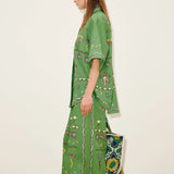 A person wears a Sun Dancer Shirt and matching wide-leg trousers, both decorated with colorful floral and geometric patterns, while holding a matching tote bag to complete the classic silhouette.