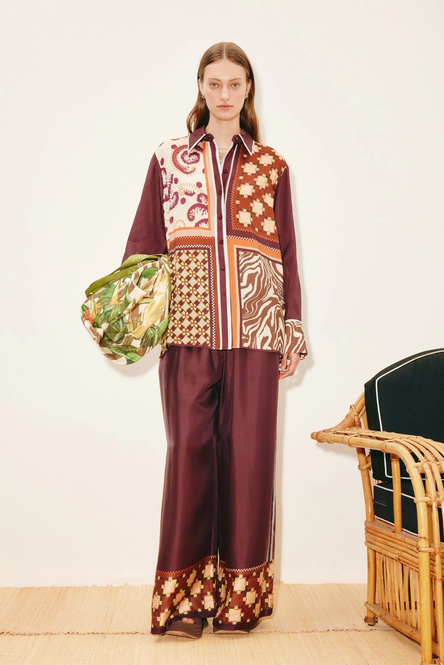 A model wears a Wilson Shirt and matching wide-leg pants in a multicolored patchwork pattern, holding a patterned green bag to create a versatile silhouette.