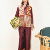 A model wears a Wilson Shirt and matching wide-leg pants in a multicolored patchwork pattern, holding a patterned green bag to create a versatile silhouette.