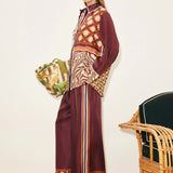 A person wears a Wilson Shirt and matching wide-leg trousers, both featuring a mix of geometric, checkered, and zebra print patterns in burgundy, brown, and cream to create a versatile silhouette.