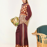 A person wears a Wilson Shirt and matching wide-leg trousers, both featuring a mix of geometric, checkered, and zebra print patterns in burgundy, brown, and cream to create a versatile silhouette.