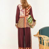 A person wears a Wilson Shirt and matching wide-leg trousers, both featuring maroon-toned panels with varied geometric and floral patterns, while holding a green patterned bag.