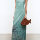 Light green strapless floor-length Amara Dress with a graphic beach scene print at the hem, styled with black heeled sandals and a brown fish-shaped handbag for special occasions.