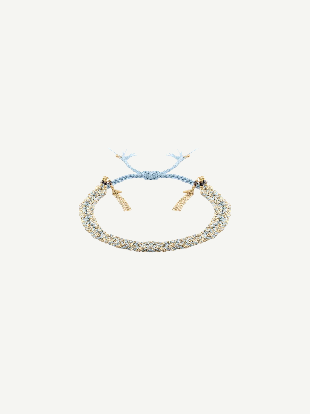 The N° 183 Braided Bracelet, crafted from luxurious amethyst silk yarn in light blue and gold threads with a radiant yellow gold finish, features elegant gold bead accents and adjustable tassel ends. It is displayed on a plain white background.