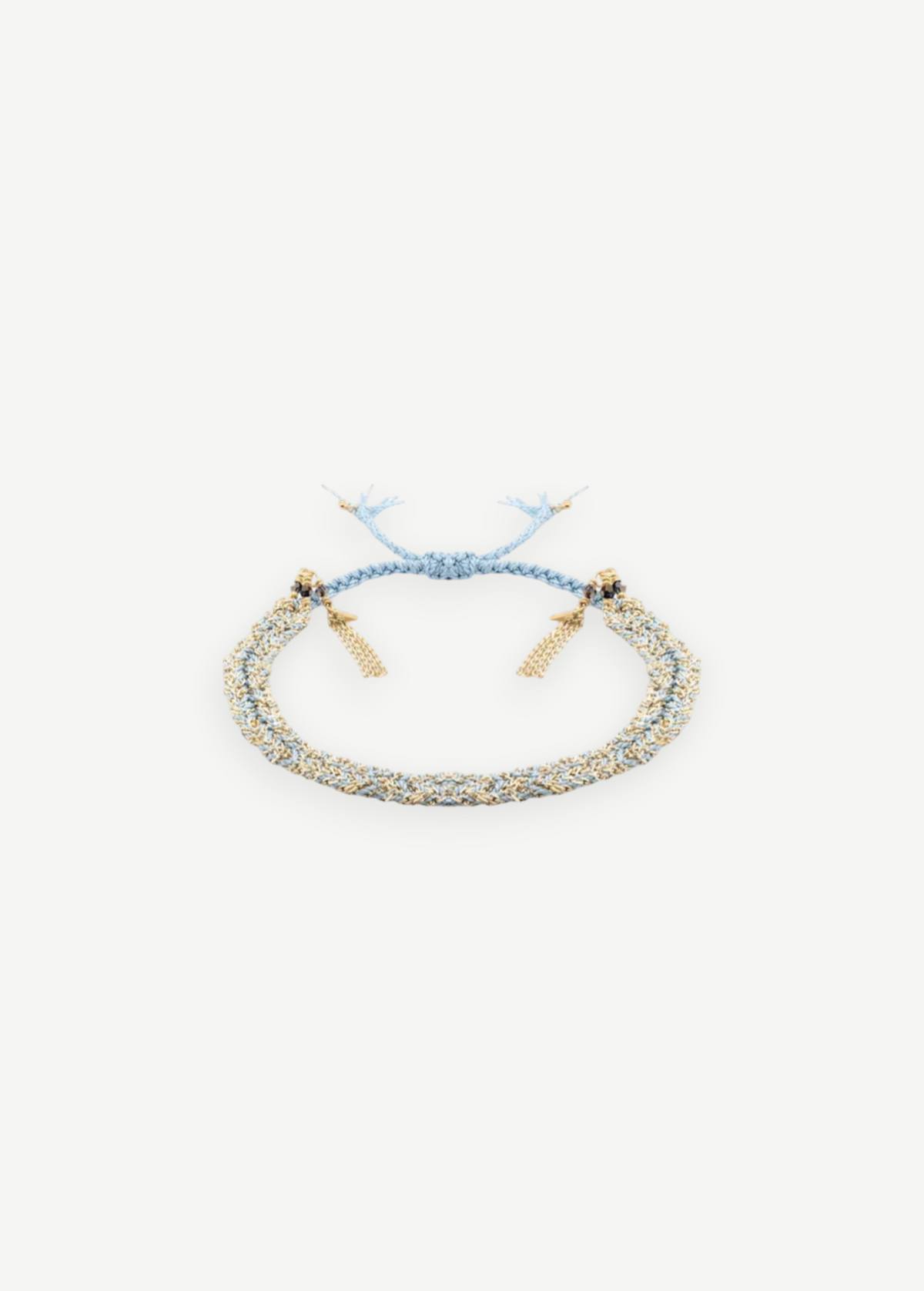 The N° 183 Braided Bracelet, crafted from luxurious amethyst silk yarn in light blue and gold threads with a radiant yellow gold finish, features elegant gold bead accents and adjustable tassel ends. It is displayed on a plain white background.