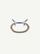The N° 183 Braided Bracelet, crafted with intertwined blue and gold threads, showcases adjustable blue tassel ends and a subtle yellow gold finish, elegantly displayed on a plain white background.
