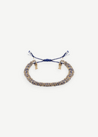 The N° 183 Braided Bracelet, crafted with intertwined blue and gold threads, showcases adjustable blue tassel ends and a subtle yellow gold finish, elegantly displayed on a plain white background.