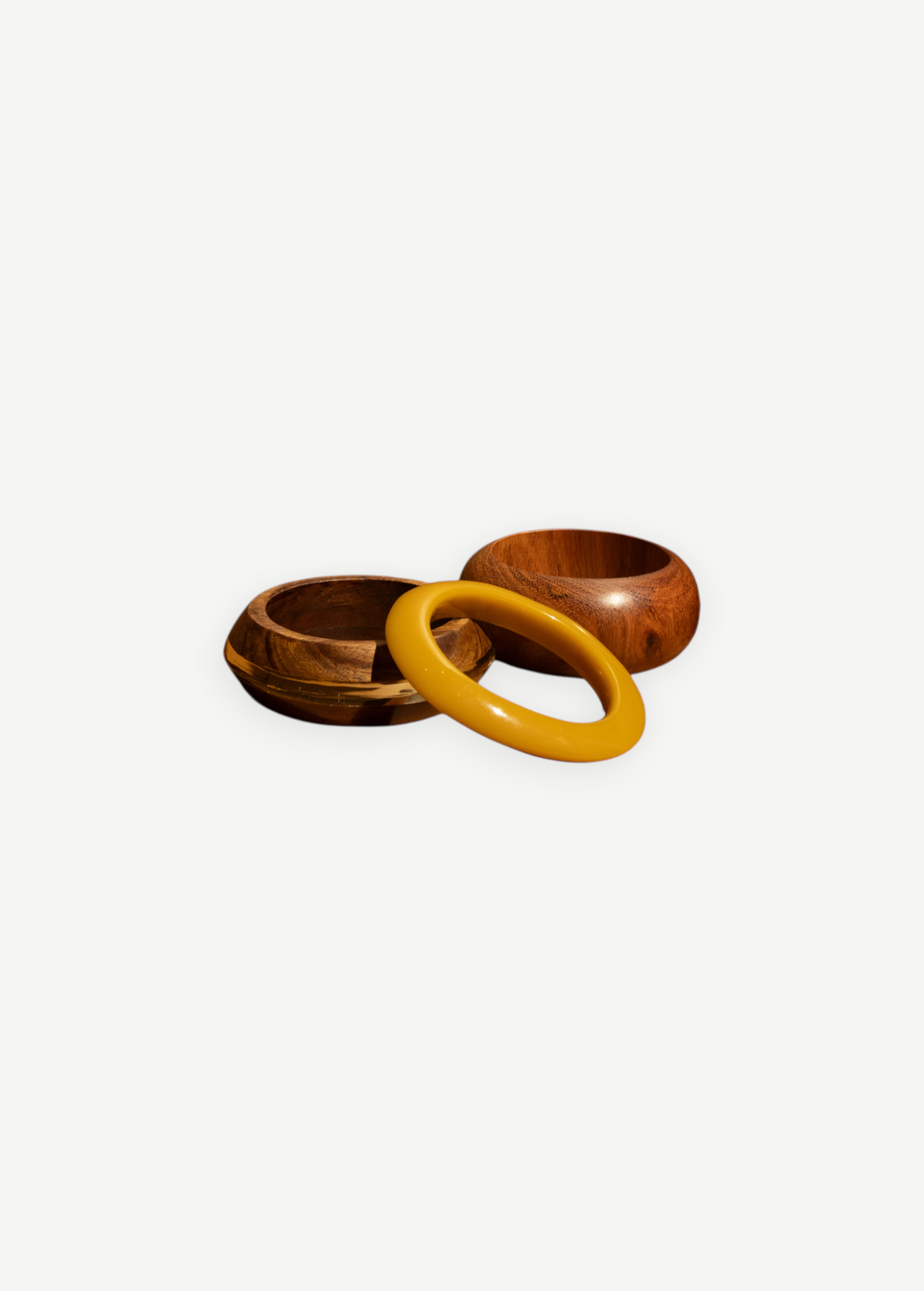 KABE SHOP INC set of three sculptural bangles featuring natural wood and smooth yellow resin in a modern design.