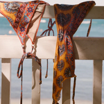 KABE SHOP INC Pietro Lizzy tie-side bikini bottoms in a retro orange and blue paisley print hanging on a white railing