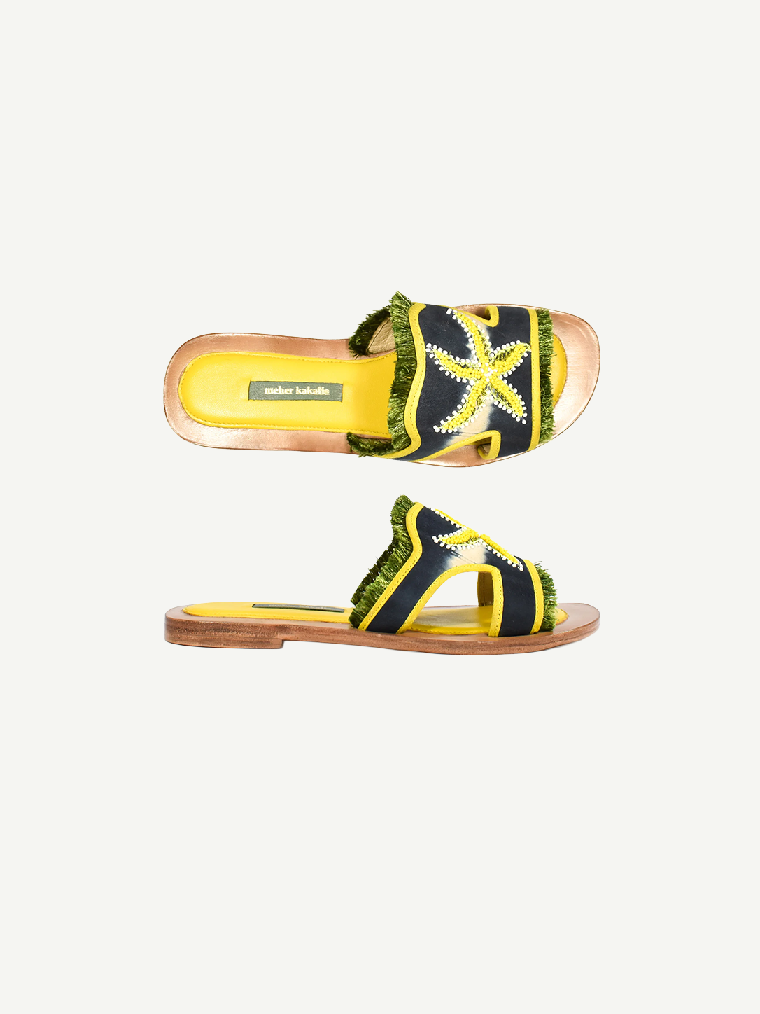Introducing the Mazu Slide: expertly crafted sustainable open-toe sandals featuring a yellow insole, a navy blue strap adorned with green fringed trim, and a striking yellow and white hand-embroidered starfish design on the upper strap—perfect for making an eco-conscious style statement.