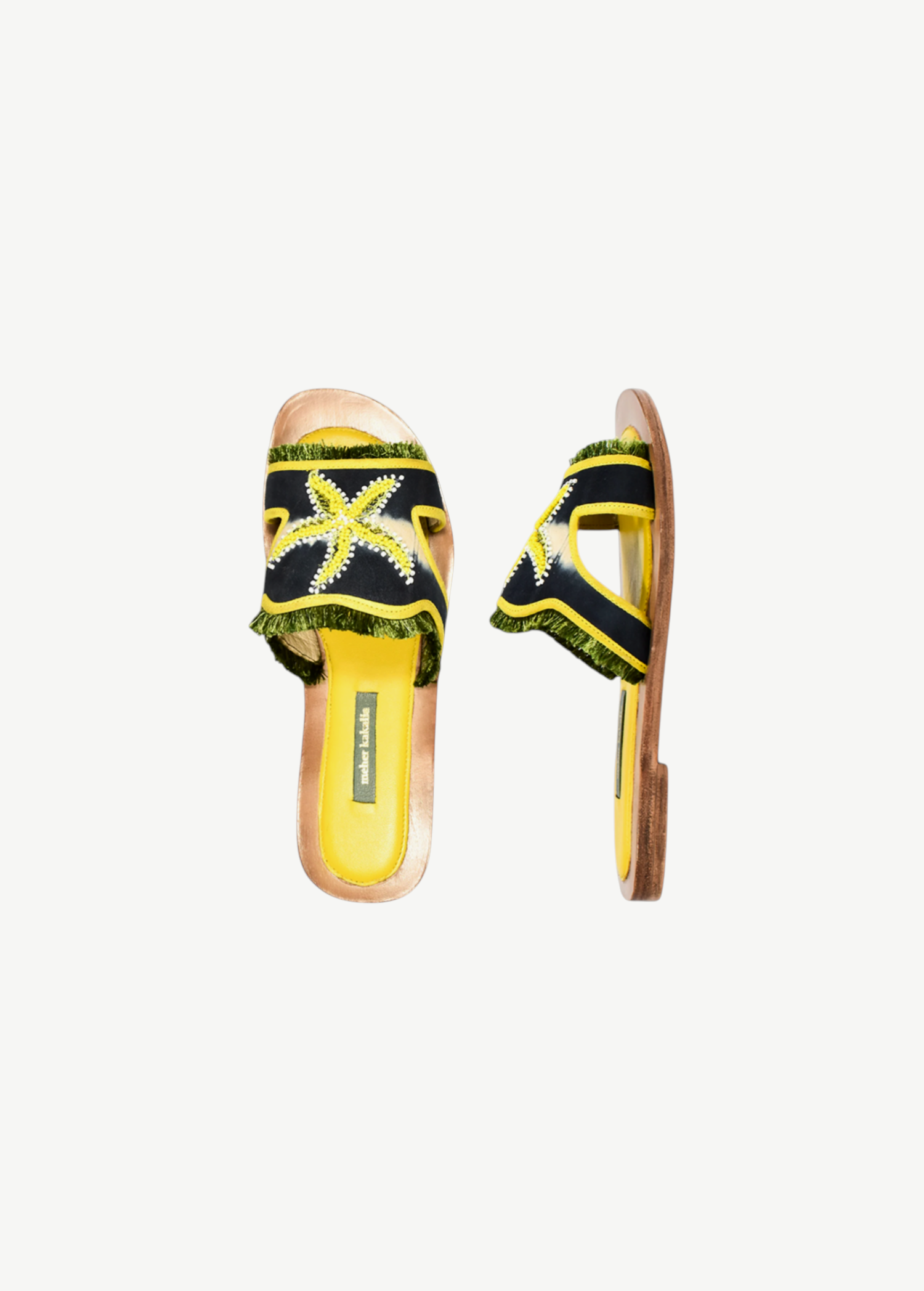 Introducing the Mazu Slide: expertly crafted sustainable open-toe sandals featuring a yellow insole, a navy blue strap adorned with green fringed trim, and a striking yellow and white hand-embroidered starfish design on the upper strap—perfect for making an eco-conscious style statement.