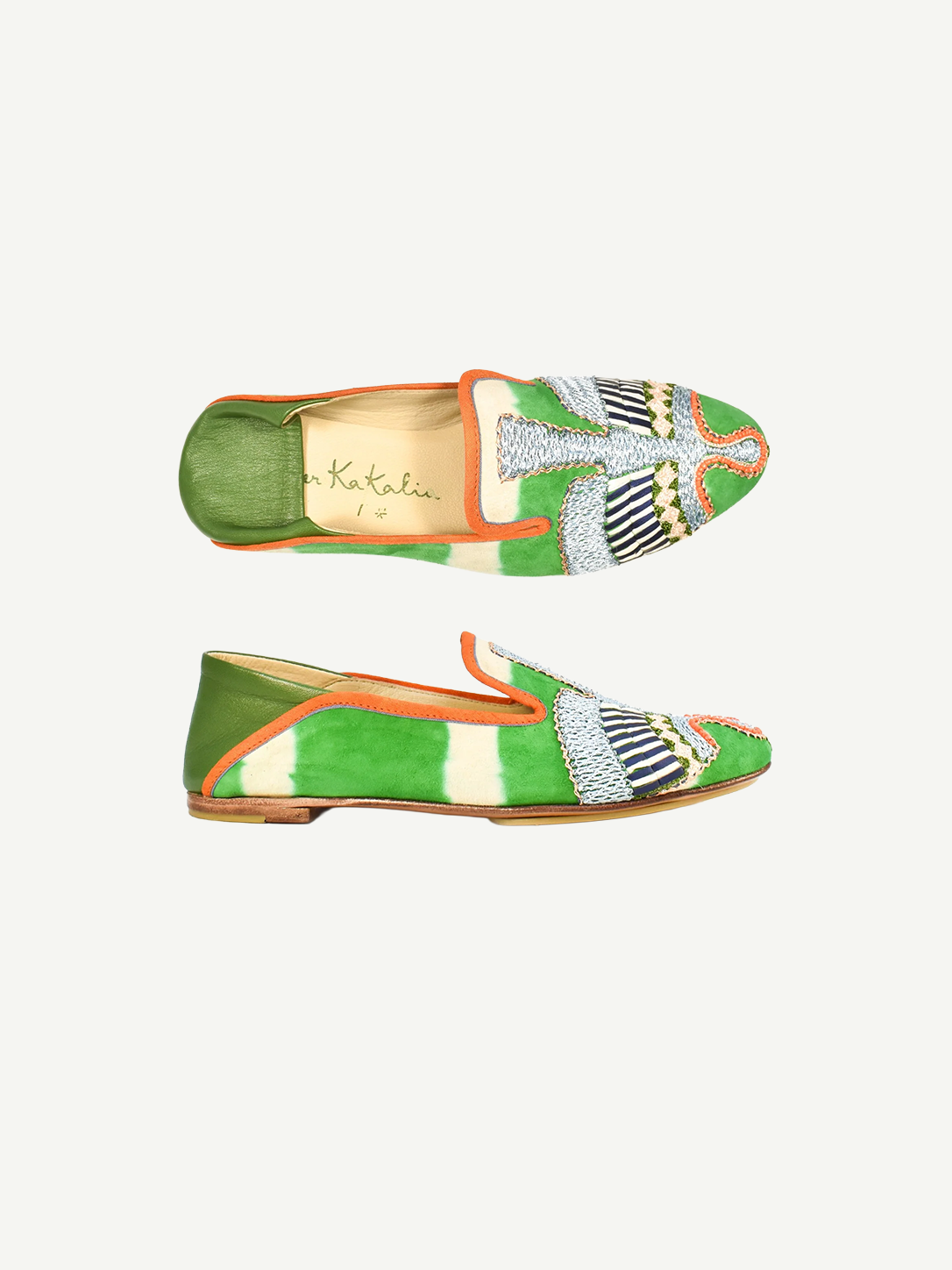 Two green and orange Anzu Moccasin shoes with intricate hand-embroidered beaded designs on the toes, displayed on a white background. The tan insoles complement geometric and wing-like patterns in white, blue, and black beadwork. These elegant slip-ons showcase exquisite moccasin craftsmanship for a truly unique finish.