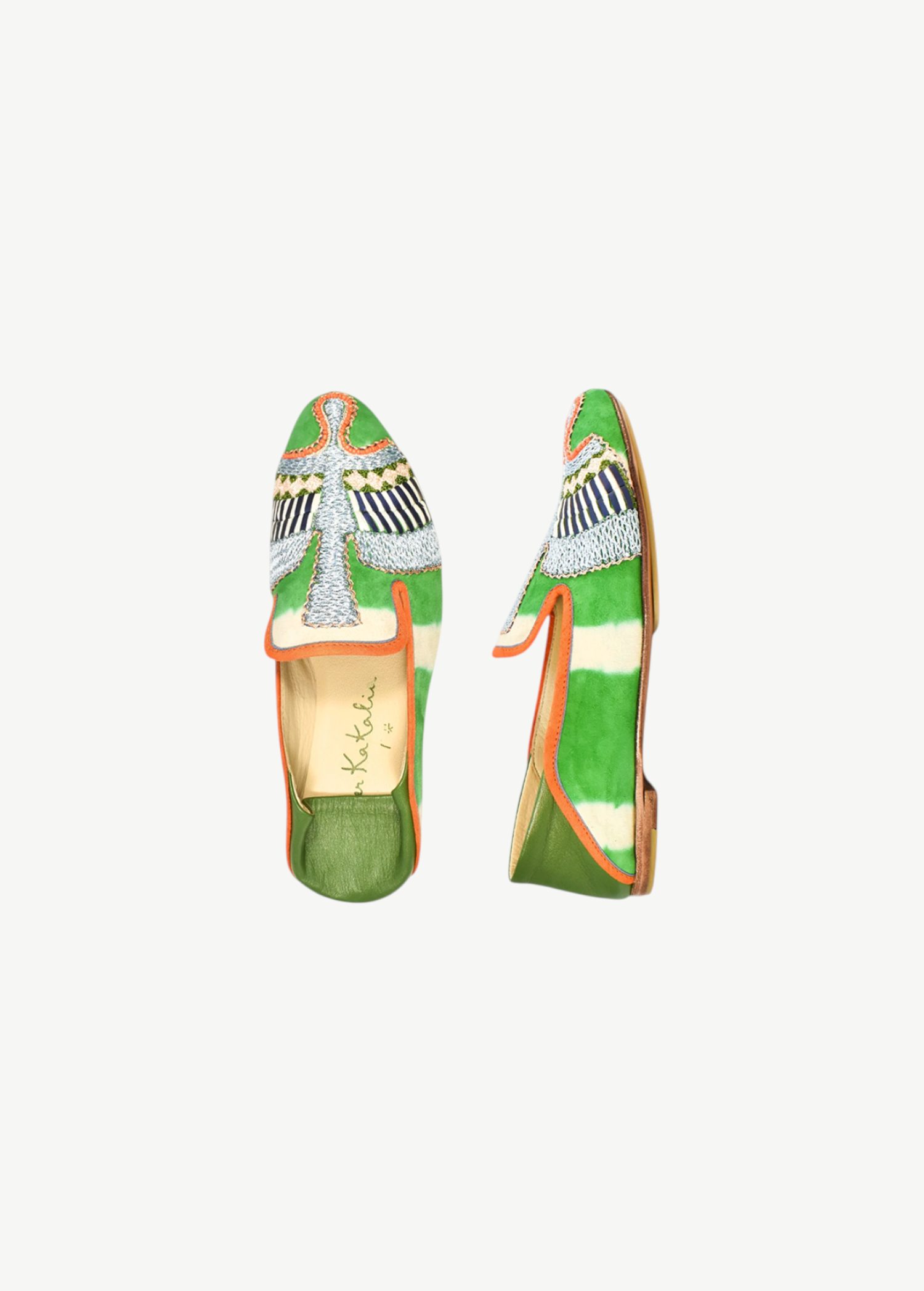 Two green and orange Anzu Moccasin shoes with intricate hand-embroidered beaded designs on the toes, displayed on a white background. The tan insoles complement geometric and wing-like patterns in white, blue, and black beadwork. These elegant slip-ons showcase exquisite moccasin craftsmanship for a truly unique finish.