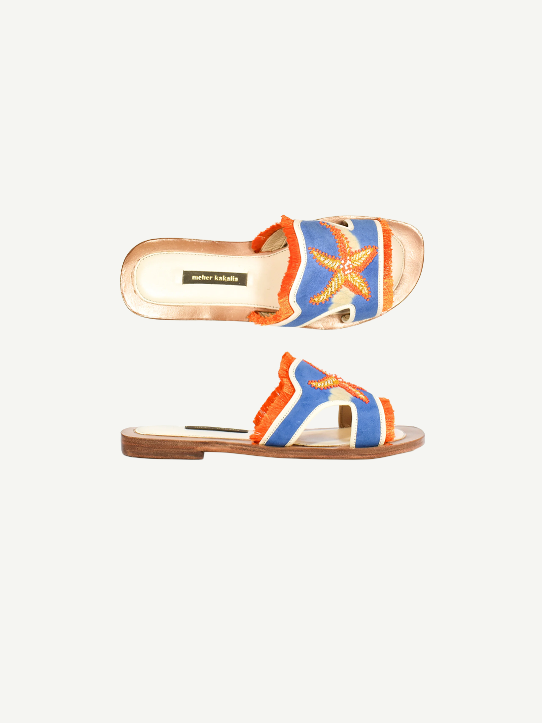 Introducing the Mazu Slide: a pair of hand-embroidered leather slip-on sandals featuring blue and orange accents, playful fringe trim, and a decorative starfish adorned with shell and bead details on the upper strap. Showcasing Silk Route’s artisan craftsmanship, these slides blend unique textures with coastal-inspired embellishments for a truly distinctive look.