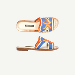 Introducing the Mazu Slide: a pair of hand-embroidered leather slip-on sandals featuring blue and orange accents, playful fringe trim, and a decorative starfish adorned with shell and bead details on the upper strap. Showcasing Silk Route’s artisan craftsmanship, these slides blend unique textures with coastal-inspired embellishments for a truly distinctive look.