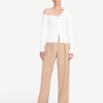 Model wearing a white KABE SHOP INC Craftsman Sweater with an off-the-shoulder neckline and tan trousers