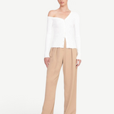 Model wearing a white KABE SHOP INC Craftsman Sweater with an off-the-shoulder neckline and tan trousers