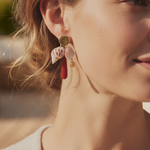 KABE SHOP INC shell earrings featuring natural shells, red gemstone drops, and gold accents worn by a woman