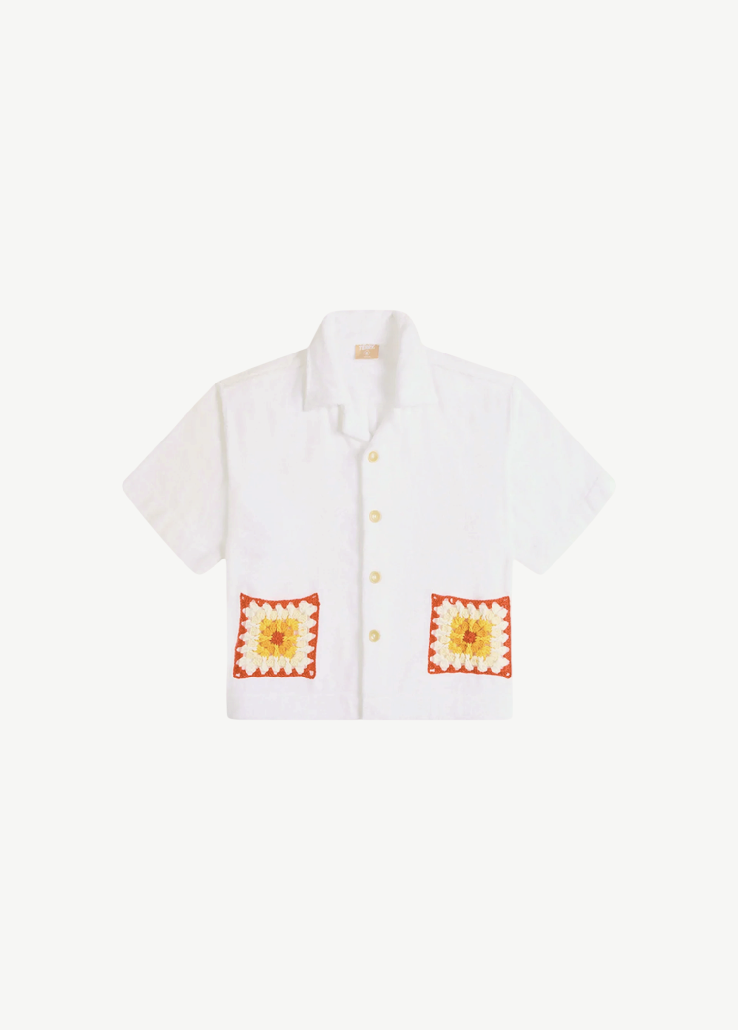 Boxy Shirt Crochet oversized white short-sleeve button-down shirt featuring two organic cotton crochet pockets with red, orange, and yellow patterns.