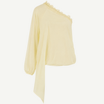 The Elia Top by De La Vali, showcased against a plain white background, features a light yellow hue and is crafted from fluid georgette. This one-shoulder silhouette is detailed with lace trim along the neckline, a single long sleeve, and an asymmetrical draped hem.