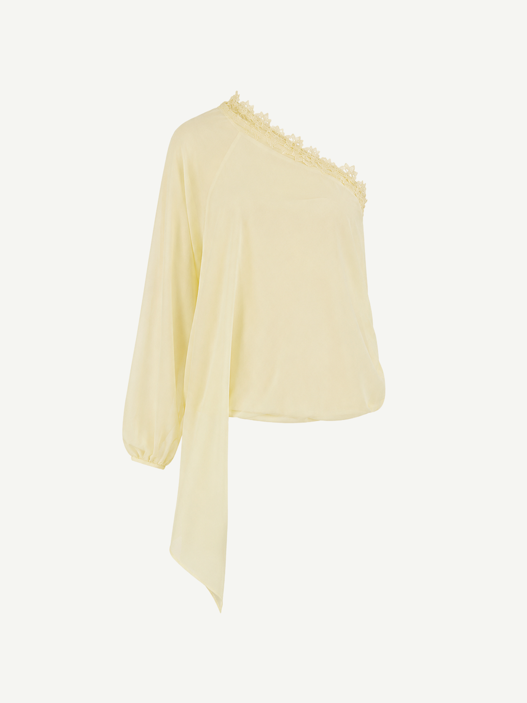 The Elia Top by De La Vali, showcased against a plain white background, features a light yellow hue and is crafted from fluid georgette. This one-shoulder silhouette is detailed with lace trim along the neckline, a single long sleeve, and an asymmetrical draped hem.