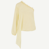 The Elia Top by De La Vali, showcased against a plain white background, features a light yellow hue and is crafted from fluid georgette. This one-shoulder silhouette is detailed with lace trim along the neckline, a single long sleeve, and an asymmetrical draped hem.