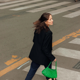 KABE SHOP INC Rosanna Bag in vibrant green handwoven buffalo leather carried by a woman walking across a city street.