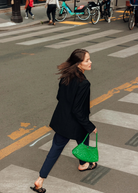 KABE SHOP INC Rosanna Bag in vibrant green handwoven buffalo leather carried by a woman walking across a city street.
