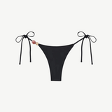 Introducing the Praia Bottom: a black bikini bottom featuring adjustable side ties and two decorative beads—one pink and one beige—on the left. Crafted from recycled polyamide, this minimal, sleek tie-bottom belongs to our eco-friendly swimwear collection, making it an ideal choice for stylish swimmers seeking sustainability.