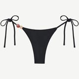 Introducing the Praia Bottom: a black bikini bottom featuring adjustable side ties and two decorative beads—one pink and one beige—on the left. Crafted from recycled polyamide, this minimal, sleek tie-bottom belongs to our eco-friendly swimwear collection, making it an ideal choice for stylish swimmers seeking sustainability.