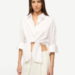 A woman wears a white Lisa Top, a button-down cropped shirt with three-quarter length sleeves and a front-tie waist, styled for everyday dressing.