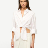 A woman wears a white Lisa Top, a button-down cropped shirt with three-quarter length sleeves and a front-tie waist, styled for everyday dressing.