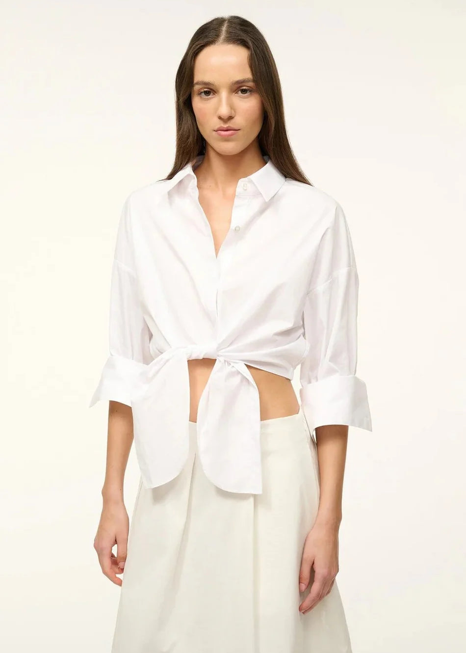 A woman wears a white Lisa Top, a button-down cropped shirt with three-quarter length sleeves and a front-tie waist, styled for everyday dressing.