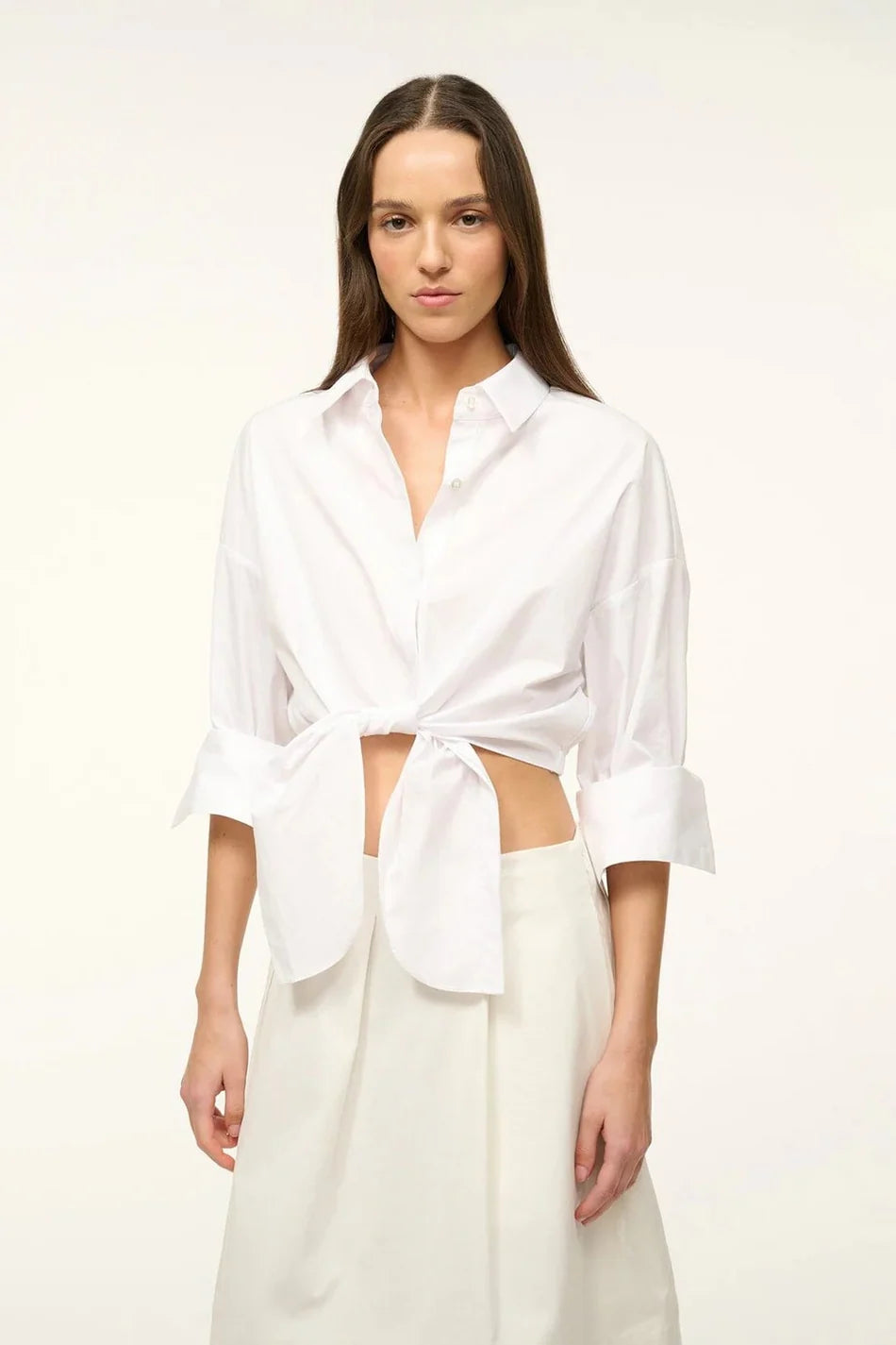 A woman wears a white Lisa Top, a button-down cropped shirt with three-quarter length sleeves and a front-tie waist, styled for everyday dressing.
