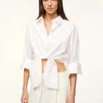 A woman wears a white Lisa Top, a button-down cropped shirt with three-quarter length sleeves and a front-tie waist, styled for everyday dressing.