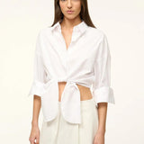 A woman wears a white Lisa Top, a button-down cropped shirt with three-quarter length sleeves and a front-tie waist, styled for everyday dressing.