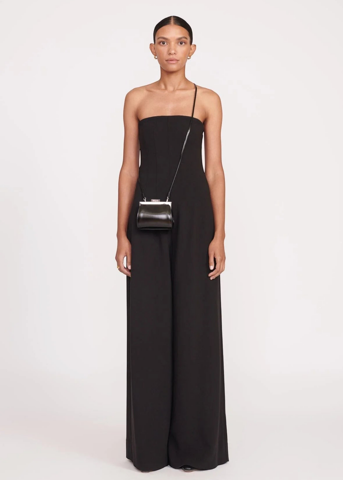 Model wearing a KABE SHOP INC Lennon convertible black bag as a crossbody accessory with a matching black jumpsuit.