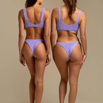 Two models wearing KABE SHOP INC Ginny bikini bottoms in textured lavender fabric with a cheeky silhouette.