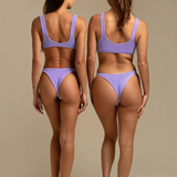 Two models wearing KABE SHOP INC Ginny bikini bottoms in textured lavender fabric with a cheeky silhouette.