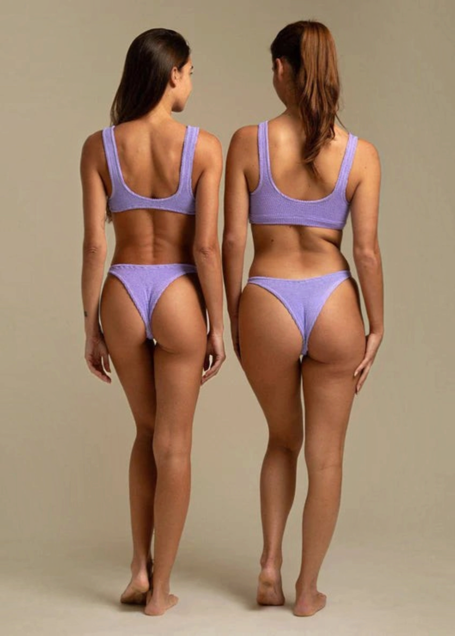 Two models wearing KABE SHOP INC Ginny bikini tops in textured lavender fabric, back view showing sporty silhouette.