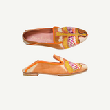 Two orange Anzu Moccasins featuring intricate pink, yellow, and gold beaded embroidery on the uppers are displayed side by side on a white background. These hand-embroidered moccasins showcase artful craftsmanship and style, making them a unique statement piece.