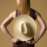 KABE SHOP INC Cajas wide brim straw hat with beaded trim held behind the back by a woman in a brown dress
