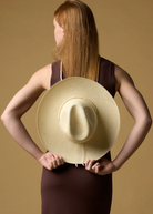 KABE SHOP INC Cajas wide brim straw hat with beaded trim held behind the back by a woman in a brown dress