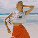 KABE SHOP INC Dolce skirt in vibrant orange worn by a blonde model holding a soccer ball on a sunny beach