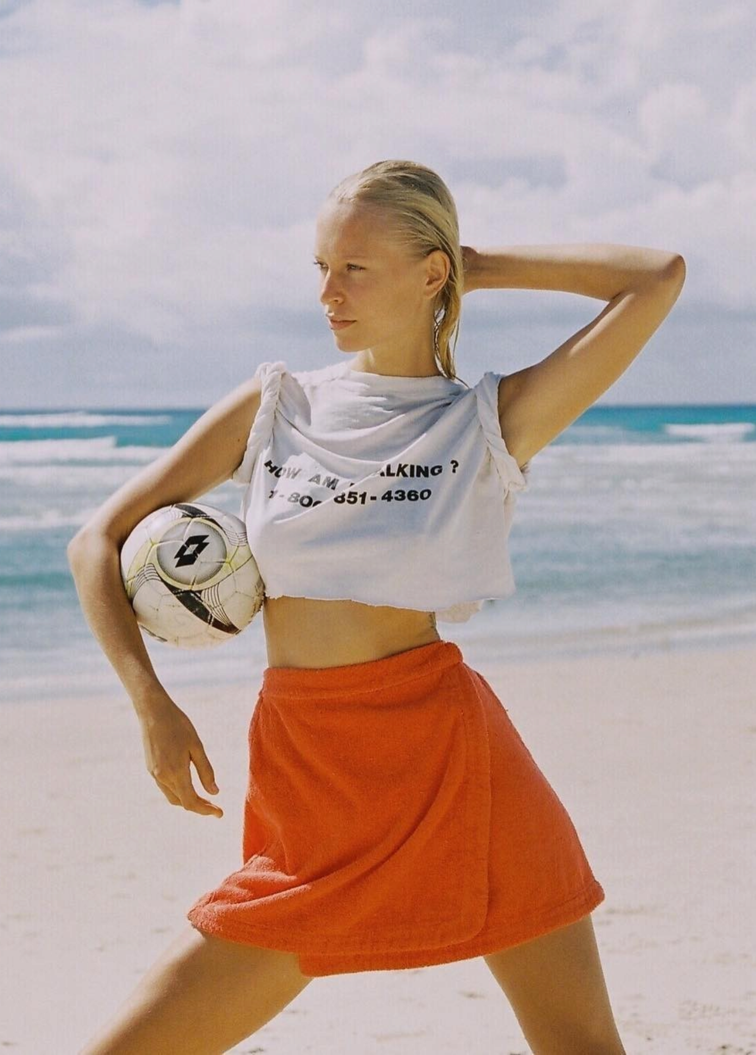 KABE SHOP INC Dolce skirt in vibrant orange worn by a blonde model holding a soccer ball on a sunny beach